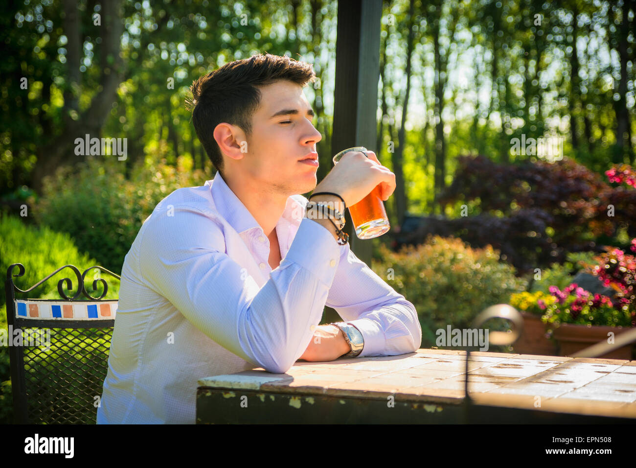 Hübscher junger Mann sitzt allein am Tisch draußen im Park oder Natur, mit Glas Soda-Getränke Stockfoto