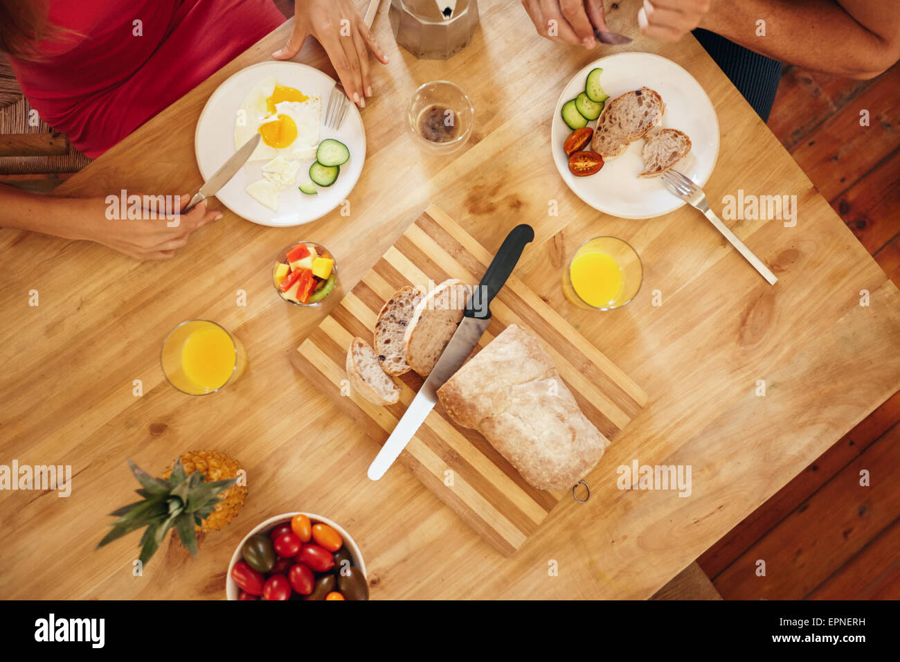 Draufsicht eines Paares, ein gesundes Frühstück zu Hause essen. Frühstückstisch mit Brotlaib auf Schneidebrett, Obst, juic Stockfoto