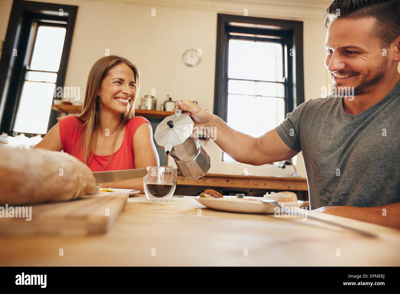Innenaufnahme junger Mann gießt Kaffee in eine Tasse mit seiner Freundin frühstücken in der Küche zu Hause. Lächelnde junge Paar Stockfoto