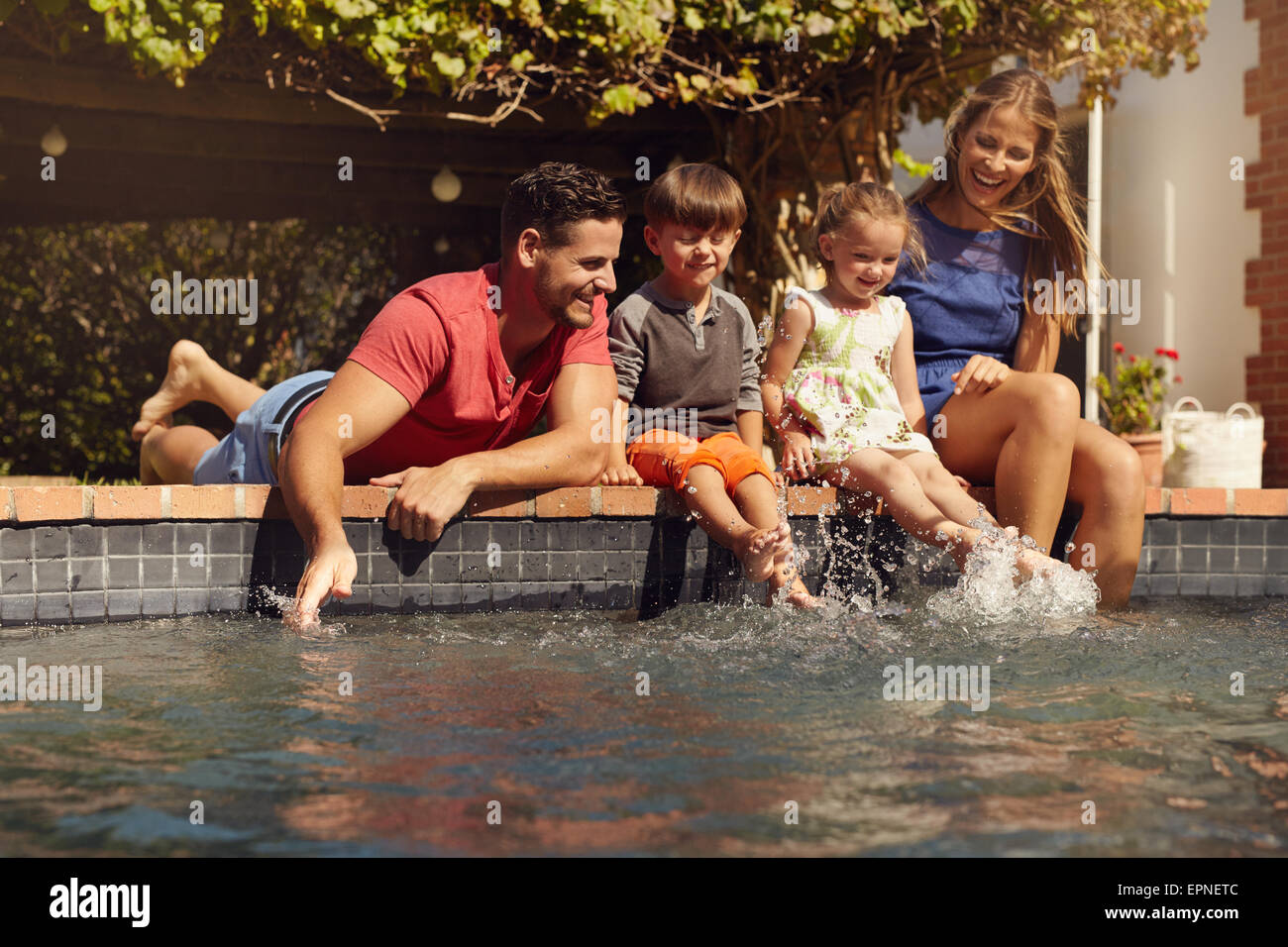 Kaukasische Familie Spaß von ihrem Pool. Glückliche junge Familie Spritzwasser mit Händen und Beinen beim Sitzen am Rand Stockfoto