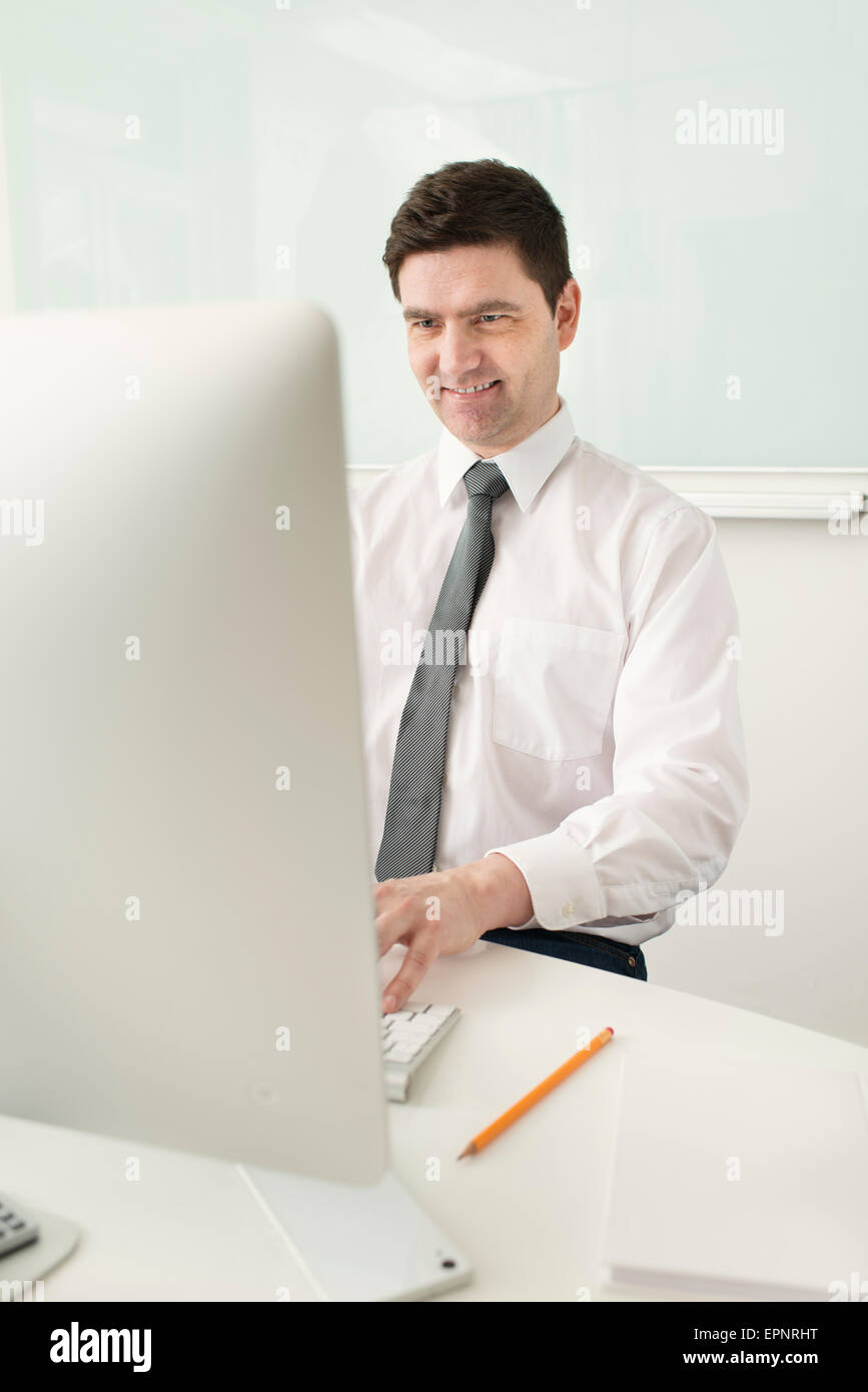 Lächelnd Geschäftsmann sitzen durch Schreibtisch, arbeiten mit Computern im Büro. Stockfoto