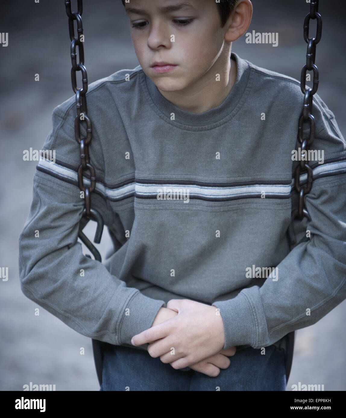 Ein kleiner Junge sitzt alleine auf einer Schaukel blickte. Stockfoto