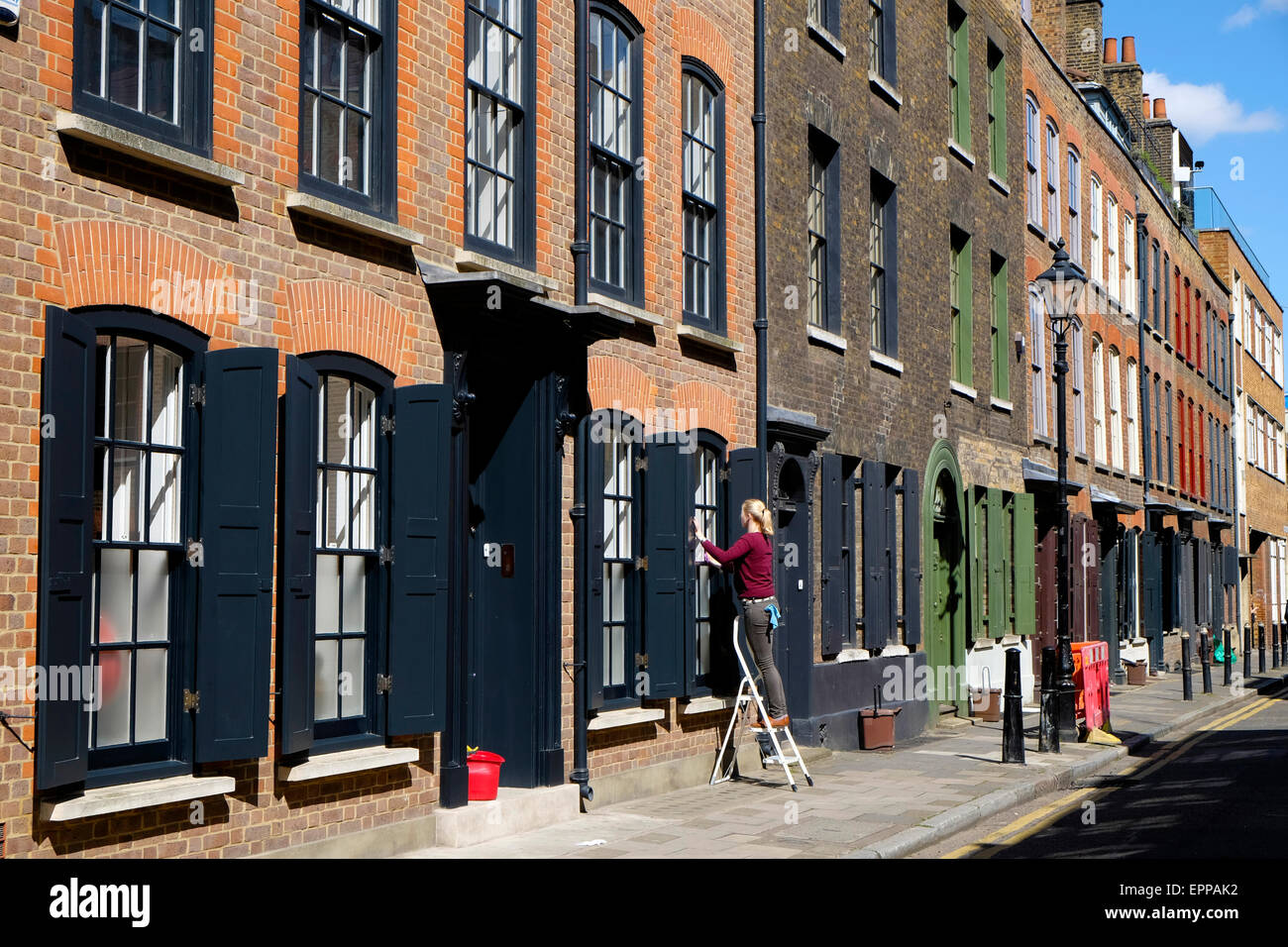 Eine Frau stand auf einer Leiter Fensterputzen vor einem Haus in Wilkes Street Shoreditch East London E1 in Shoreditch UK KATHY DEWITT Stockfoto