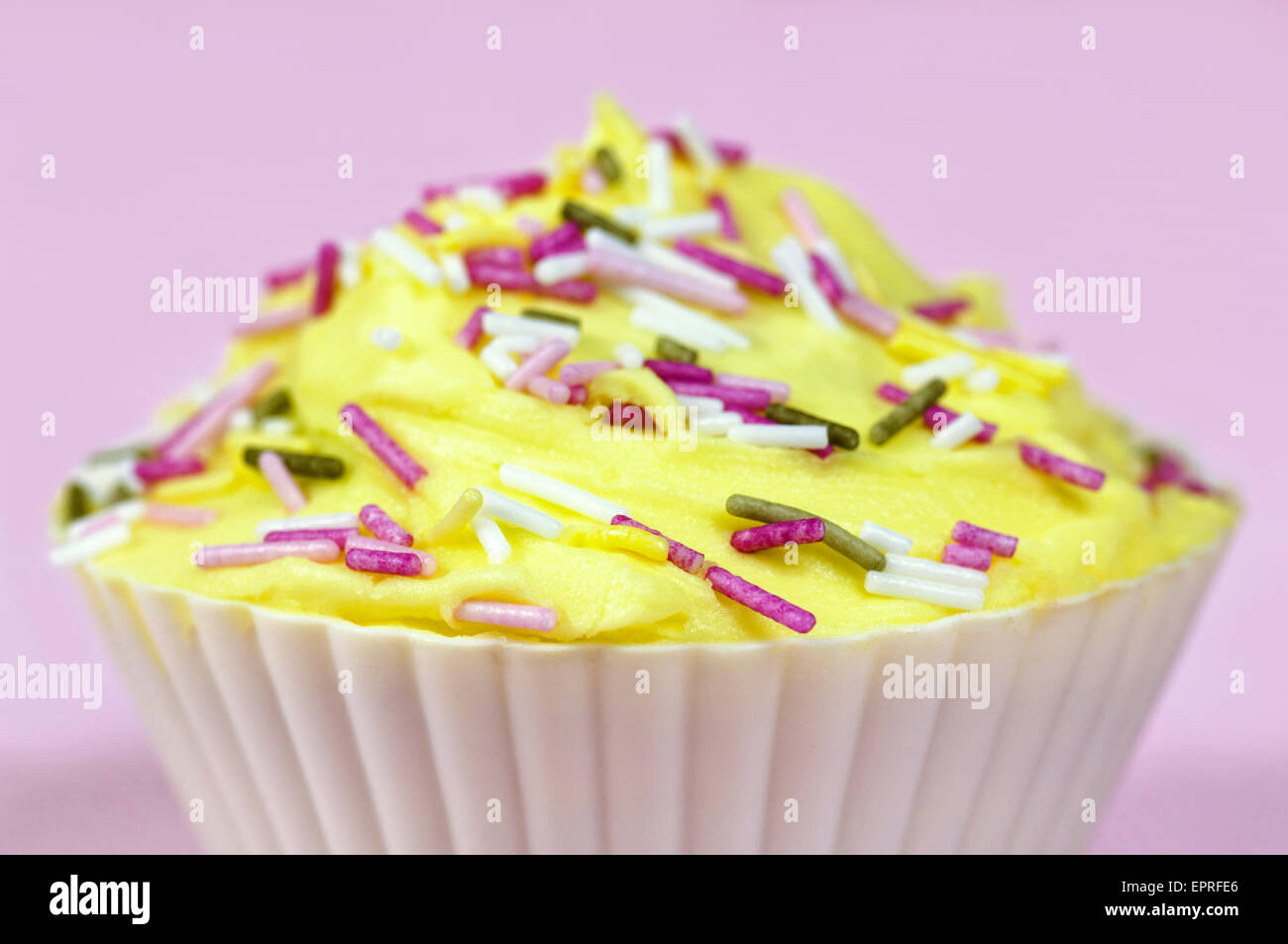 Ziemlich bunt dekorierten Kuchen oder Fee Kuchen mit gelber Zuckerguss und bunte Streusel auf einem rosa Hintergrund Stockfoto