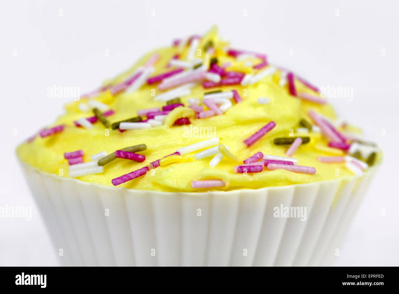 Ziemlich bunt dekorierten Kuchen oder Fairy Cake mit gelben Glasur und bunten Streuseln auf weißem Hintergrund Stockfoto