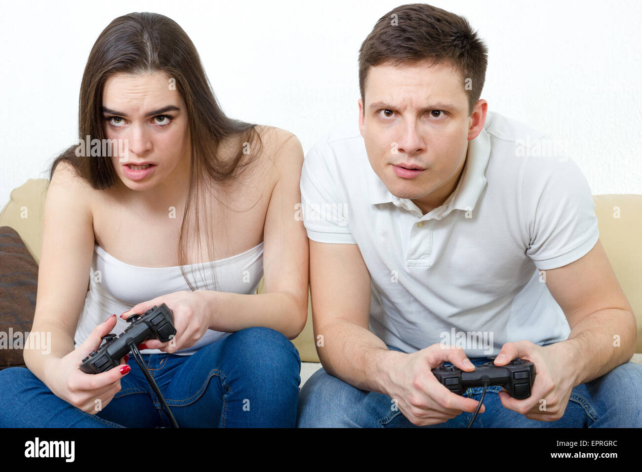 Junge Paar im Wohnzimmer sitzen und spielen Videospiele auf Konsole oder pc mit Joysticks während der Suche im Bildschirm oder Fernseher. Lifestyl Stockfoto