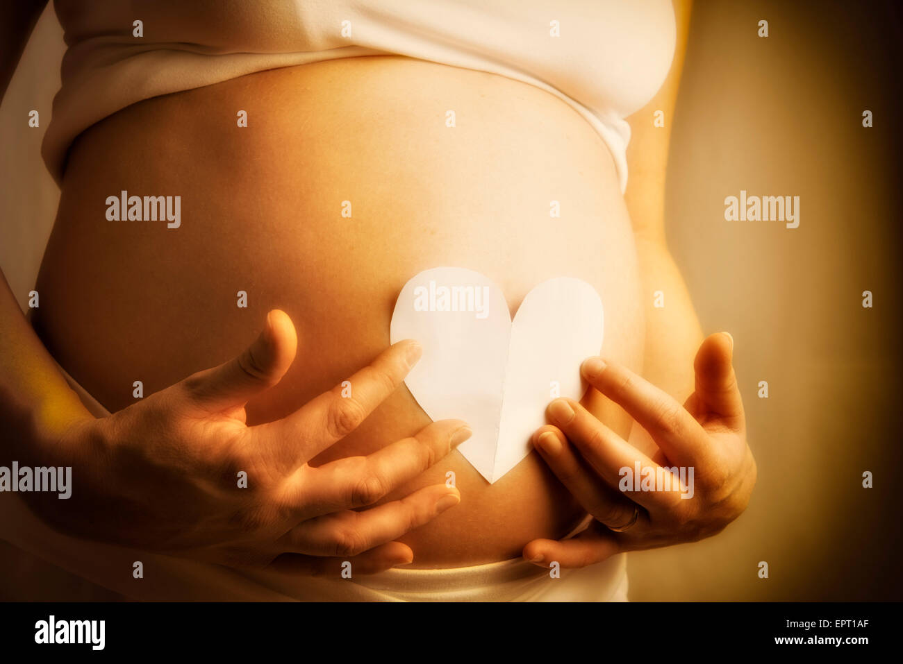 Schwangere Frau mit Papierherz auf ihrem Baby-Bauch Stockfoto
