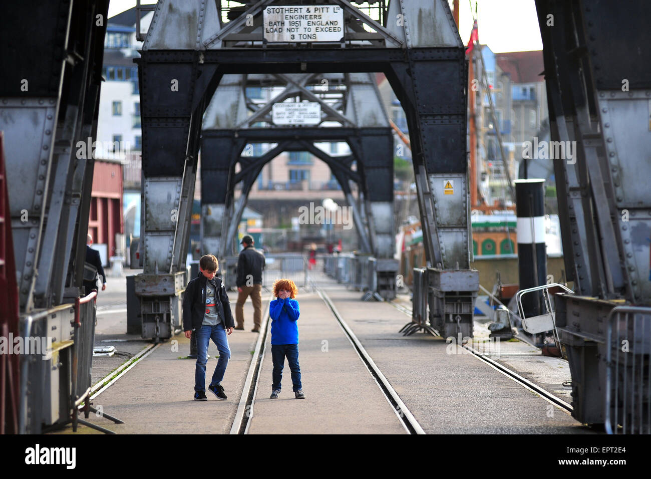 Zwei Jungs gehen unter die erhaltene Ladung Krane entlang der Hafenpromenade in Bristol. Stockfoto