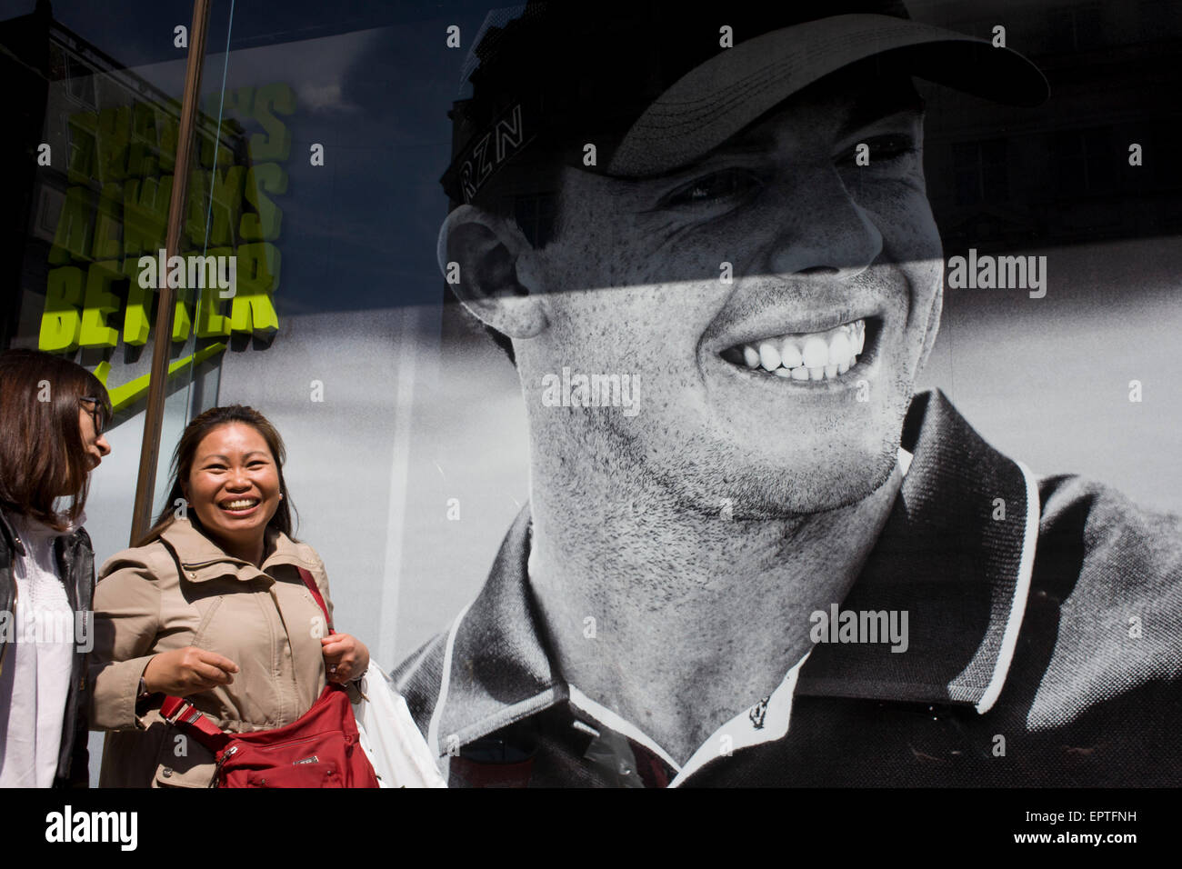 Lächelnde Frau und Freund übergeben ein Nike-Einzelhandel-Plakat der nördlichen irischen Golfer Rory McIlroy, im Zentrum von London. Stockfoto