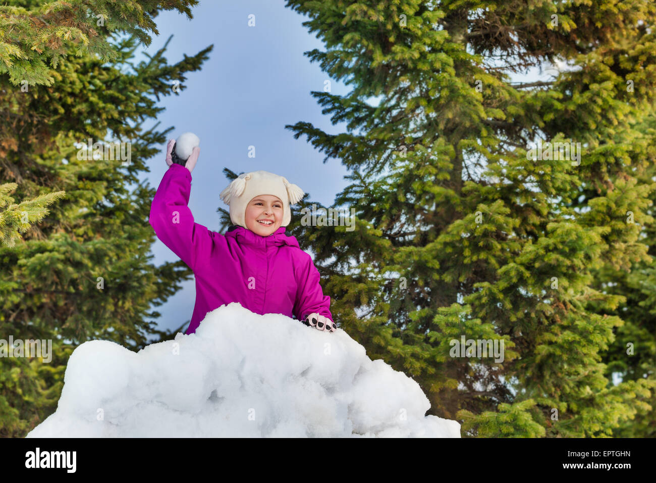 Schönes Mädchen hält Schneeball hinter Schneewand Stockfoto