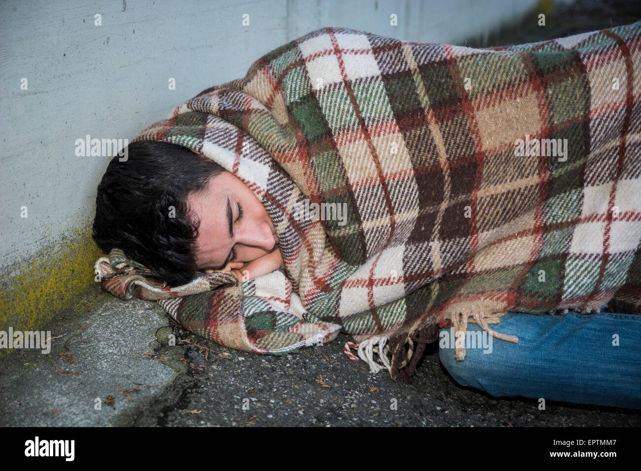 Junge männliche Bettler schlafen auf Stadt Bürgersteig mit Decke auf seinen Schultern Stockfoto