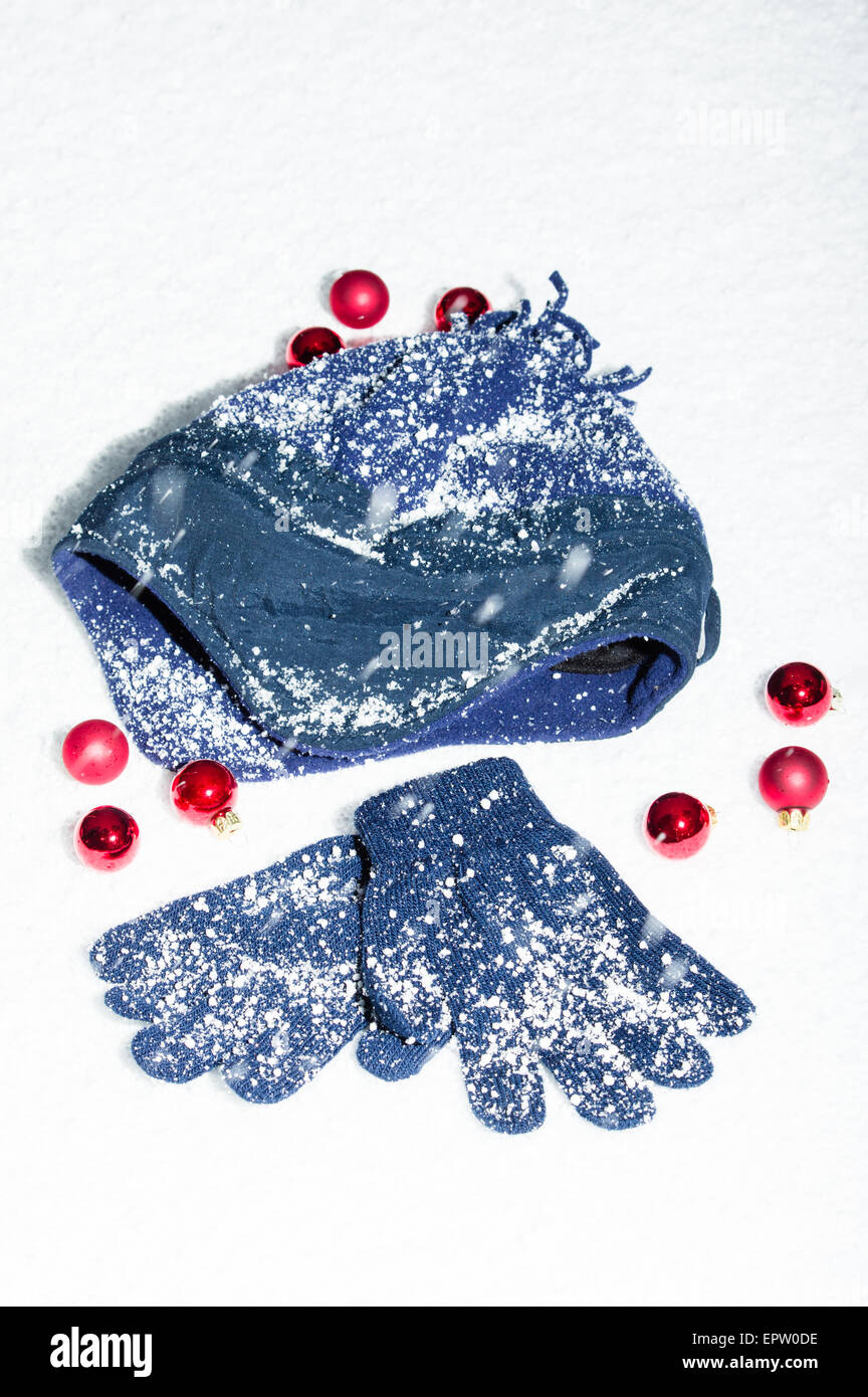 Eine Mütze und Handschuhe im Schnee mit roten Weihnachtskugeln Stockfoto