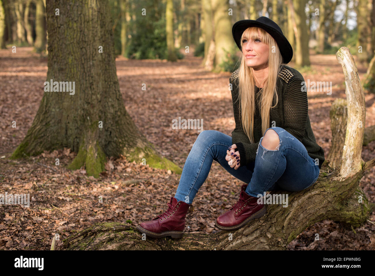 Junge Frauen in einen Hut und Freizeitkleidung sitzen auf einem Baumstamm in den Wäldern im Sonnenlicht Stockfoto