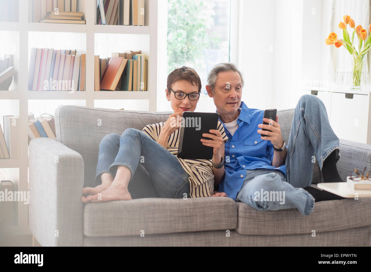 Älteres Paar Austausch von elektronischen Geräten auf sofa Stockfoto