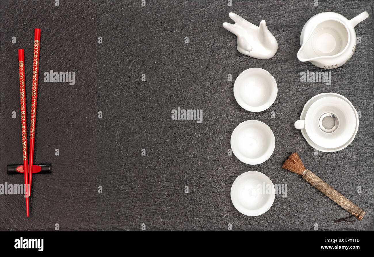 Geschirr für traditionelle asiatische Tee-Zeremonie. Teekanne, Tassen und roten Stäbchen auf schwarzem Stein Tisch Hintergrund. Stockfoto