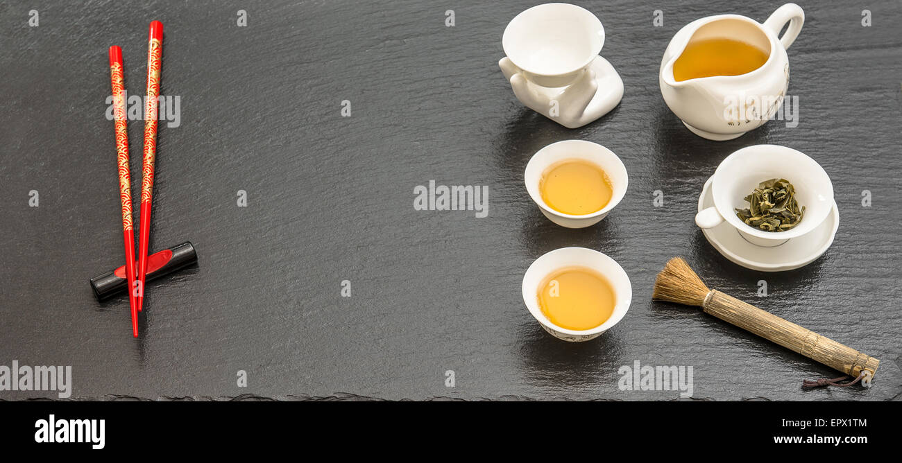 Geschirr für traditionelle asiatische Tee-Zeremonie. Teekanne, Tassen und roten Stäbchen auf schwarzem Hintergrund Stockfoto