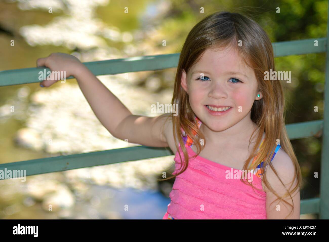 Hübsches junges Mädchen mit blauen Augen stützte sich auf Brücke mit dem Fluss im Hintergrund. Stockfoto