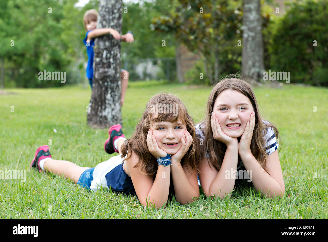 Junge Mädchen, die Verlegung auf dem Rasen, während ihre jüngere Schwester an einem Baum im Hintergrund hängt Stockfoto