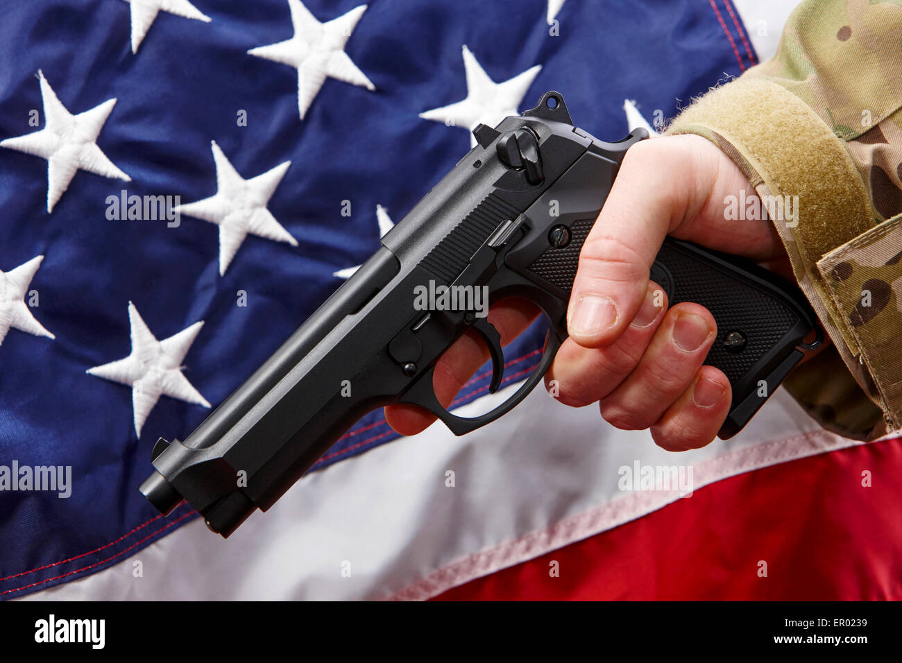 Mann in Strapazen holding Beretta Pistole vor Vereinigte Staaten von Amerika Flagge Stockfoto