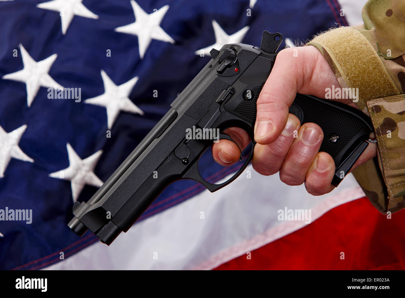 Mann in Strapazen holding Beretta Pistole mit Finger am Abzug vor Vereinigte Staaten von Amerika Flagge Stockfoto