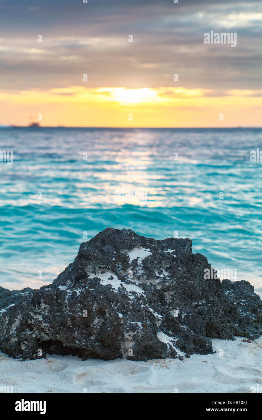Großen schwarzen Stein am weißen Sandstrand auf der tropischen Meer Sonnenuntergang Stockfoto