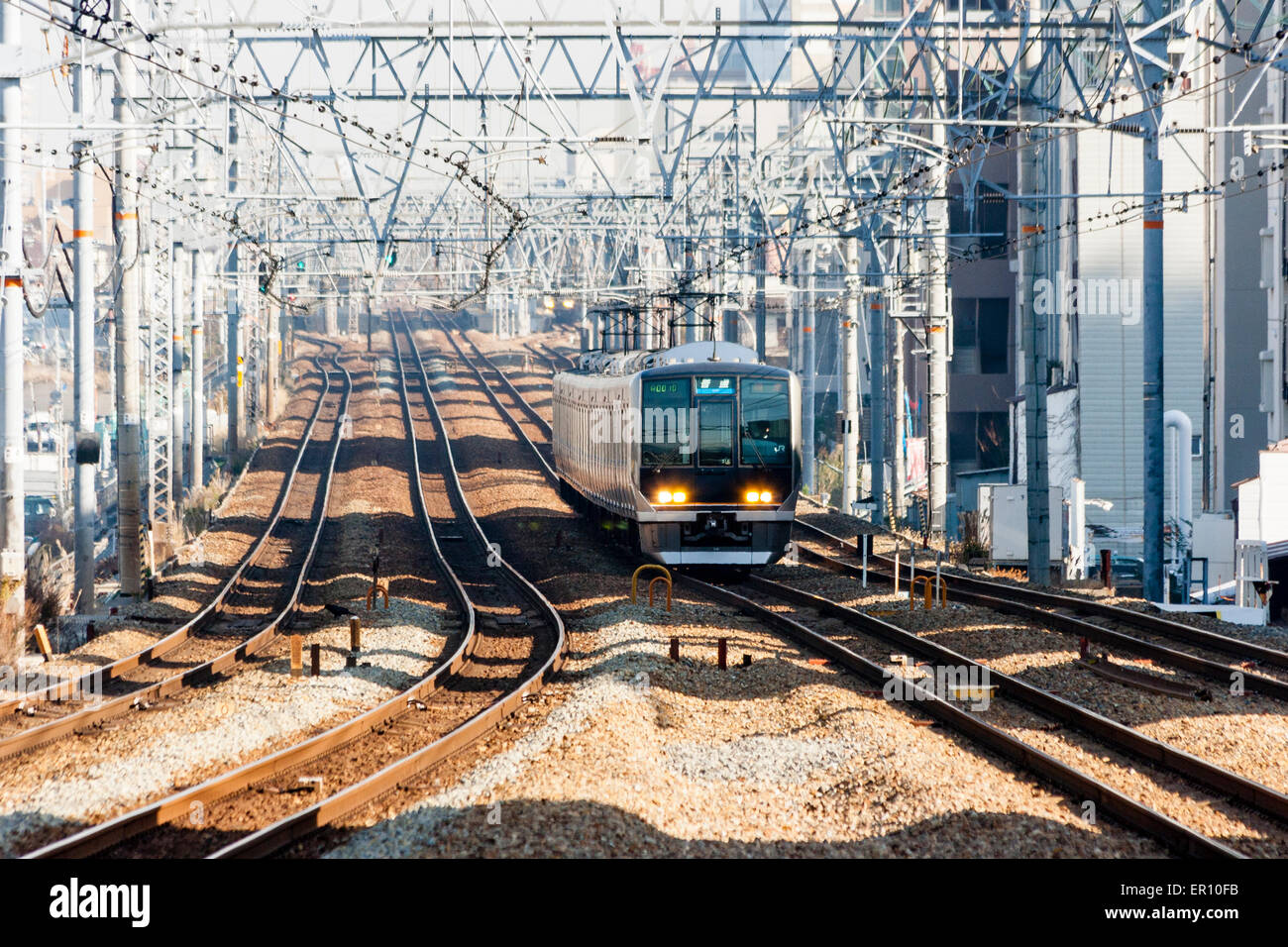 Blick auf vier Eisenbahnschienen mit elektrifizierten Obergleisen auf der Osaka-Kobe-Linie in Shukugawa. Ein Zug nähert sich. Stockfoto