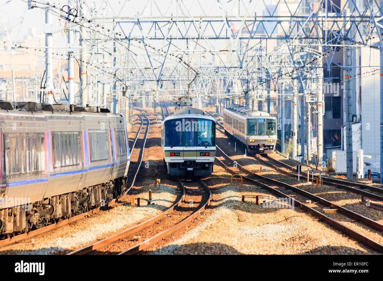 Blick auf vier Eisenbahnschienen mit elektrifizierten Obergleisen auf der Osaka-Kobe-Linie in Shukugawa. Drei Züge nähern sich. Stockfoto