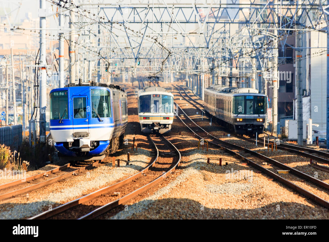 Blick auf vier Eisenbahnschienen mit elektrifizierten Obergleisen auf der Osaka-Kobe-Linie in Shukugawa. Drei Züge nähern sich. Stockfoto