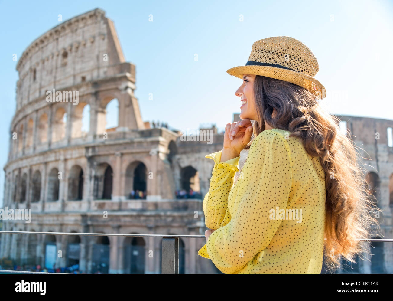 Eine Frau Tourist ist stehend, stützte sich ihr Kinn auf ihre Hände und Blick in die Ferne und lächelnd. Sie ist die Aussicht bewundern. In der Ferne, das Kolosseum an einem heißen Sommertag. Stockfoto