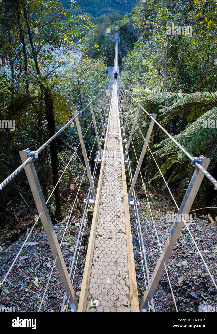 Eine weibliche Walker über eine schmale Stahl Hängebrücke über den Waiho River auf der Strecke von Roberts nach Franz Josef Gletscher NZ Stockfoto