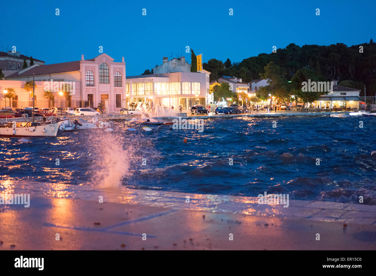 Ein Abend im Hafen von Rovinj, Kroatien, mit Spritzwasser, Wellen und eine aufgewühlte Meer in der Ferne Menschen besuchen Sie die beleuchteten Geschäfte Stockfoto