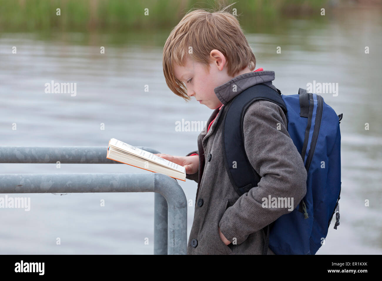 kleiner Junge liest ein Buch während des Wartens auf ein Boot Stockfoto