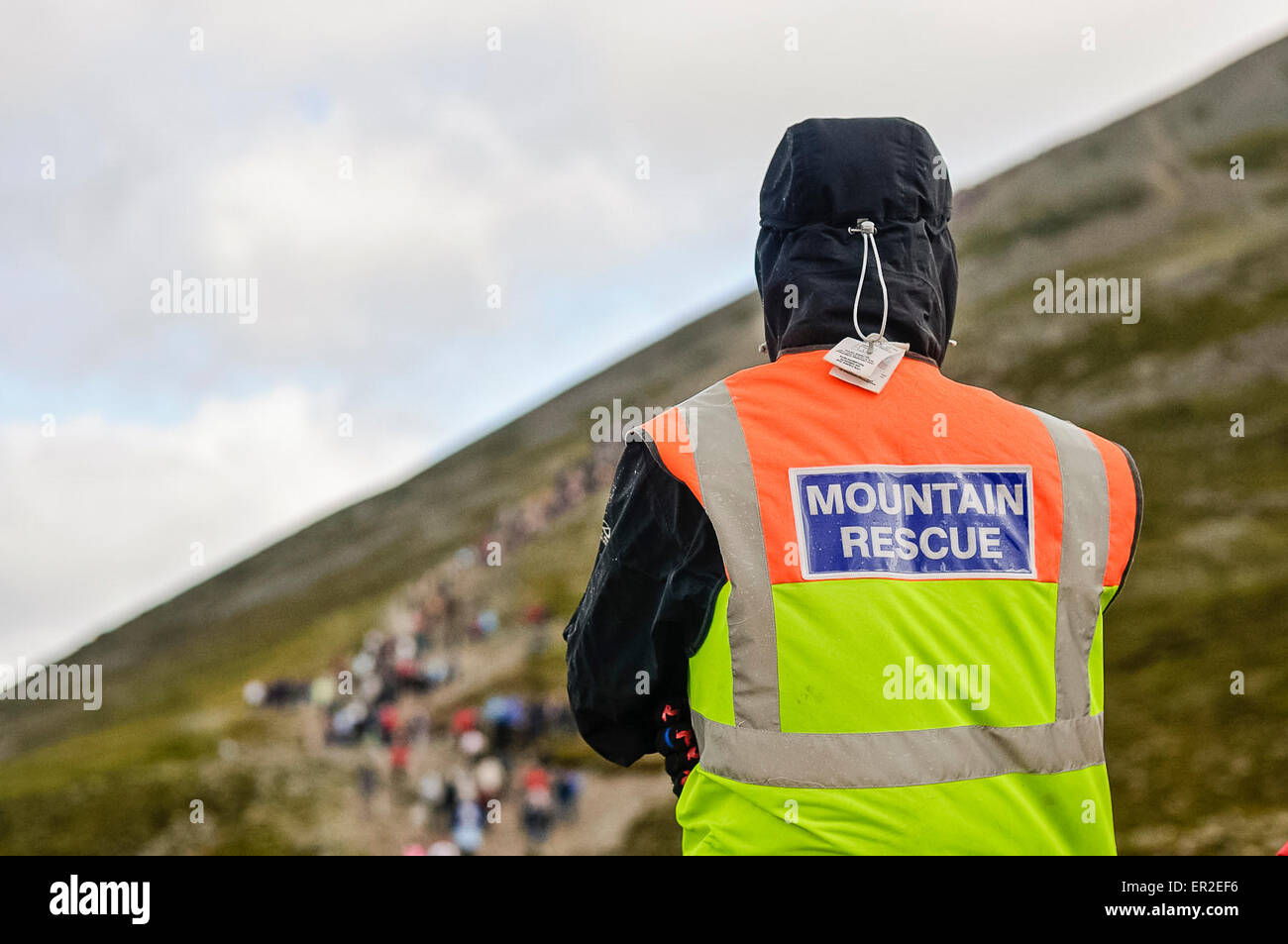 Ein Mann aus Bergrettung schaut zu, wie Hunderte von Menschen einen steilen Berg hinauf gehen Stockfoto