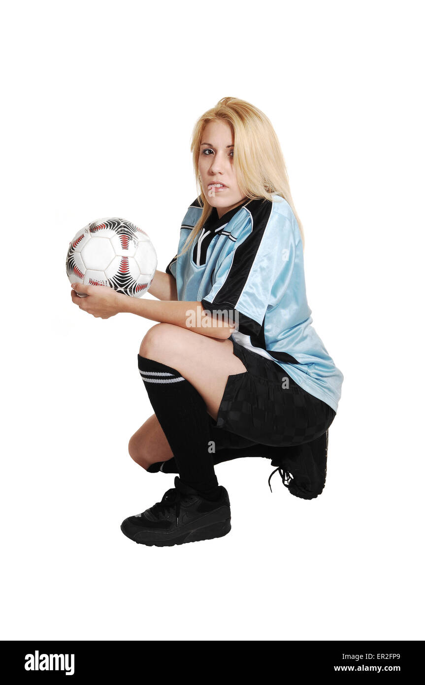 Eine blonde junge Fußball-Frau kniend im Studio in ihrem Verein einheitlich und einen Fußball für weißen Hintergrund. Stockfoto