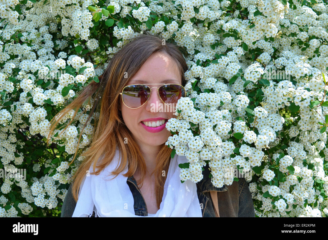 Fröhliches junges Mädchen mit Sonnenbrille posiert umgeben von Blumen Stockfoto