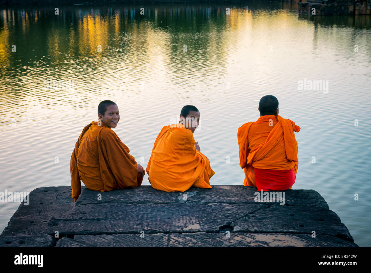 SIEM REAP, Kambodscha - 30. Oktober 2014: Anfänger buddhistische Mönche in orangefarbenen Gewändern sitzen am Rand des Grabens in Angkor Wat. Stockfoto