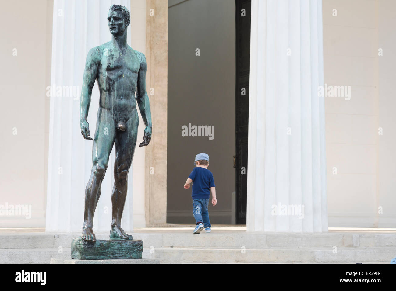 Mann und Junge, Blick auf ein Kind, das vor dem Theseus-Tempel im Volksgarten in Wien an einer Skulptur eines athletischen Mannes vorbeigeht. Stockfoto
