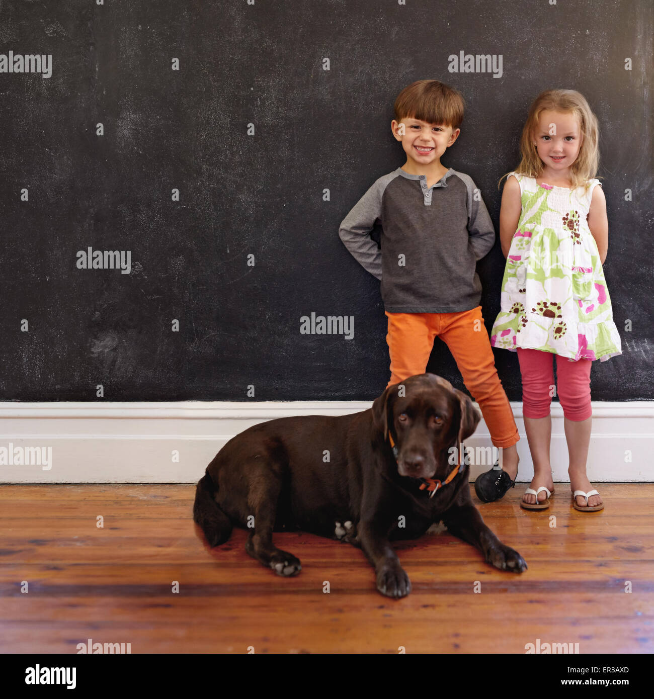 Voller Länge Schuss von lächelnden kleinen Jungen und Mädchen stehen neben Hund zu Hause. Labrador Retriever sitzend im Stock mit Kinder stan Stockfoto