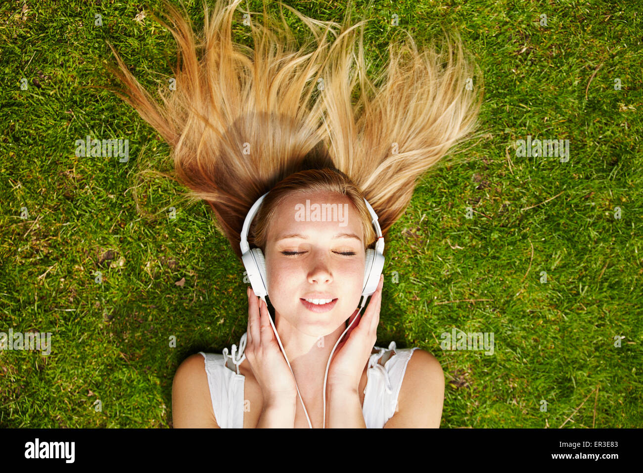 Anhören von Musik-streaming mit Kopfhörer im Sommer auf einer Wiese Mädchen Stockfoto