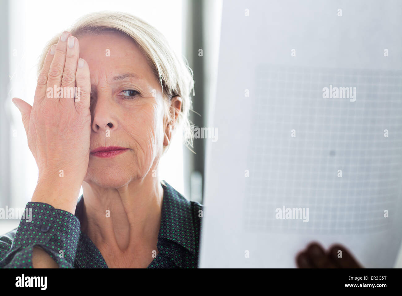Ältere Frau betrachten ein Amsler-Gitters, Makula-Degeneration zu erkennen. Stockfoto