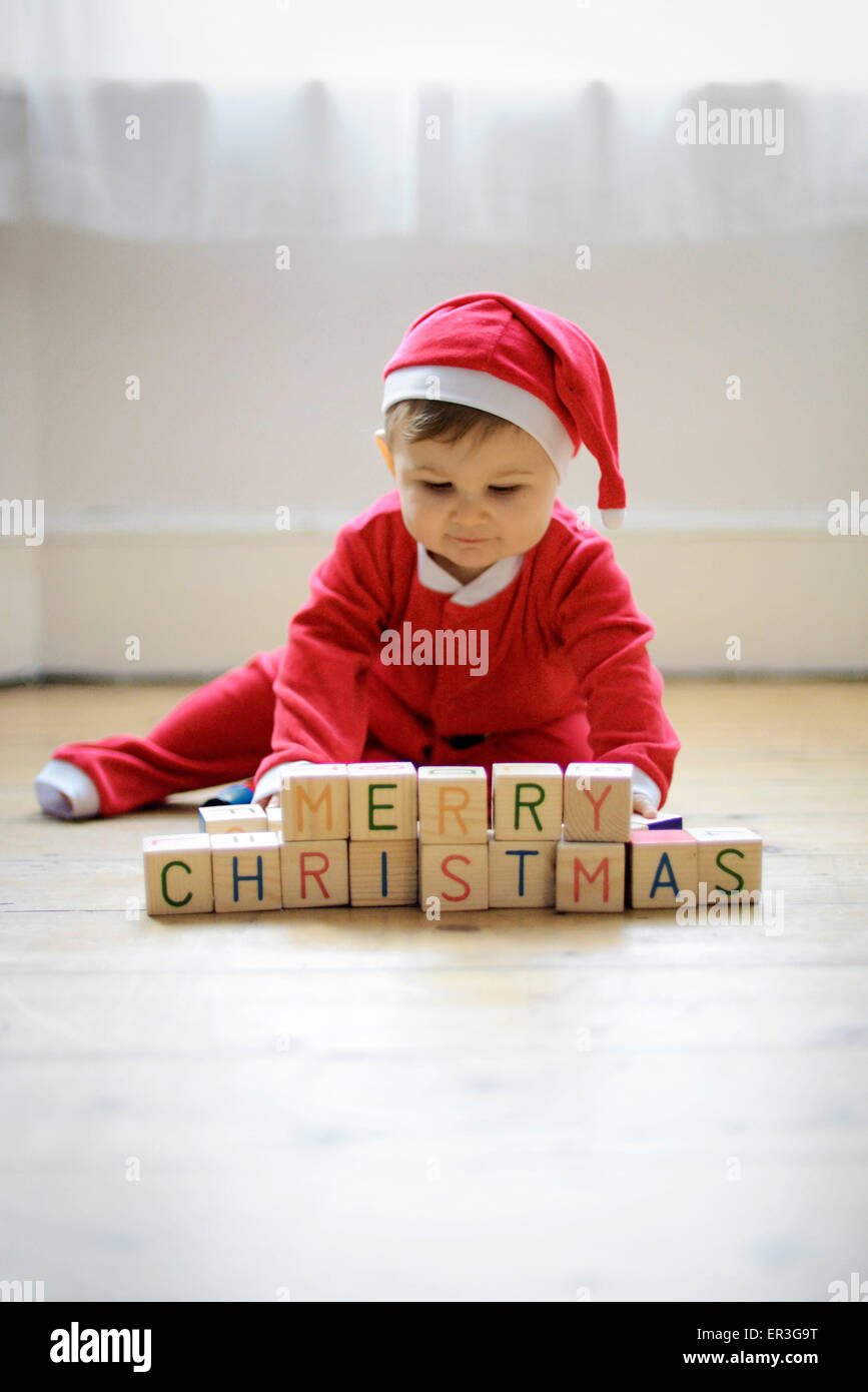 Baby Boy mit Klötzchen lesen 'Frohe Weihnachten' als Weihnachtsmann verkleidet Stockfoto