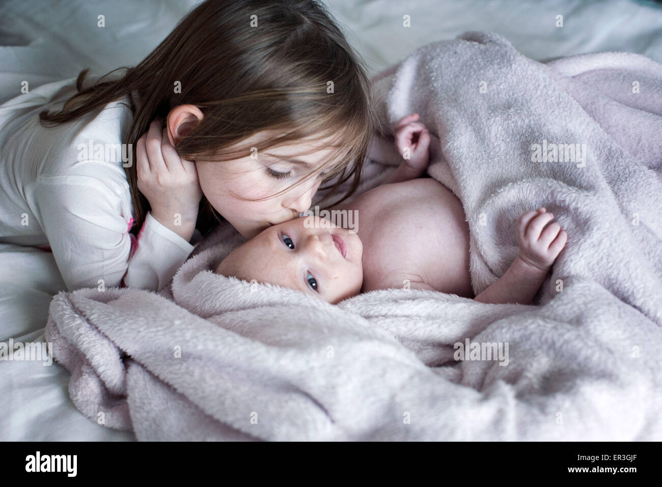 Kleines Mädchen küssen Baby Bruder Wange auf Bett Stockfoto