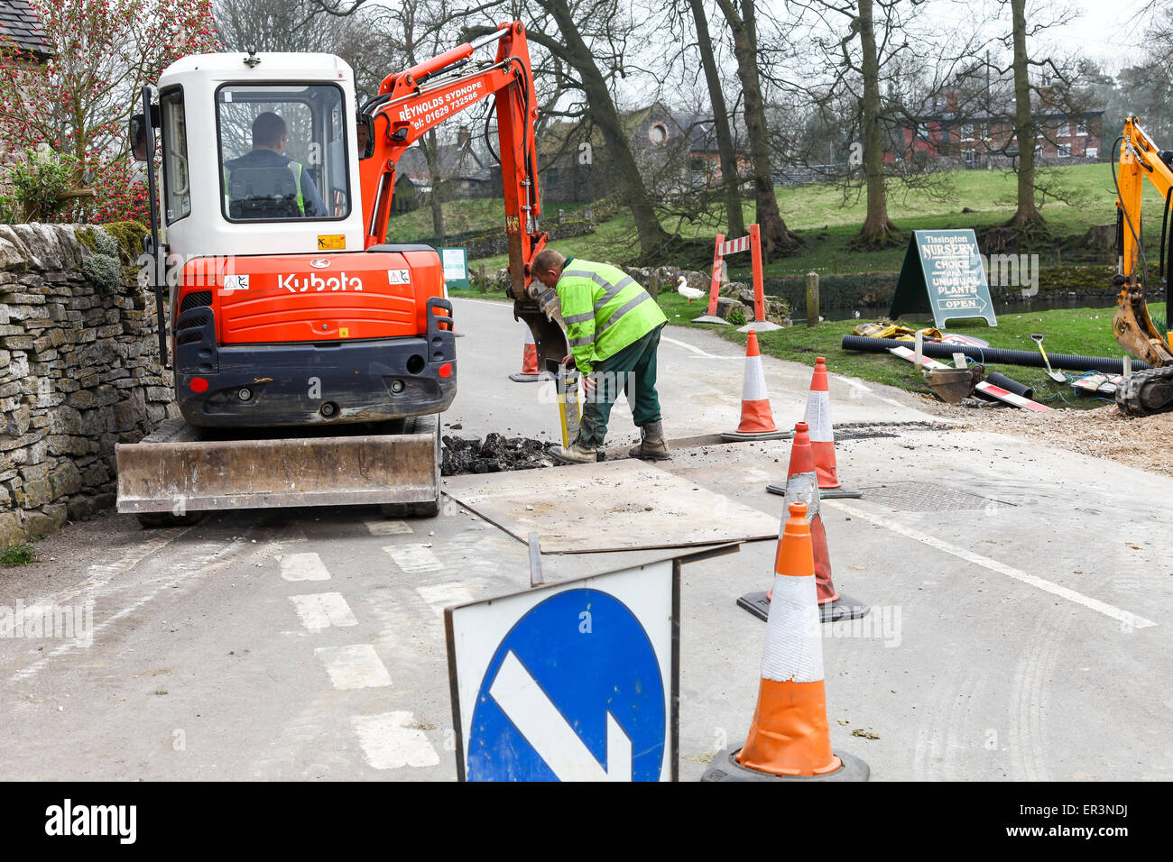 Zwei Arbeiter einen Graben über eine Straße mit einem mechanischen Bagger Stockfoto