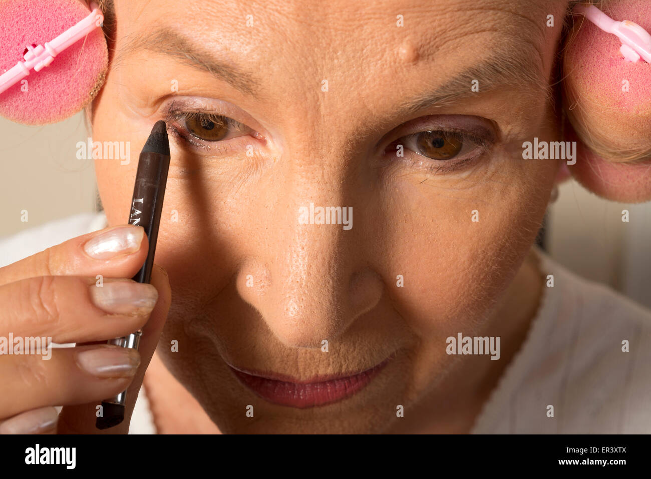 Frau in Lockenwickler eyeliner auftragen Stockfoto