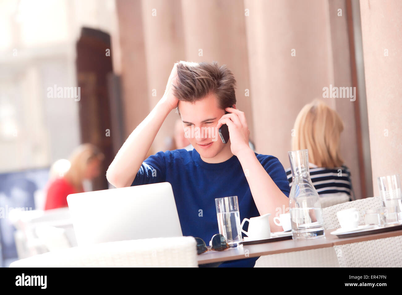 Junger Mann sitzt im äußeren Kaffeehaus reden über Handy Stockfoto