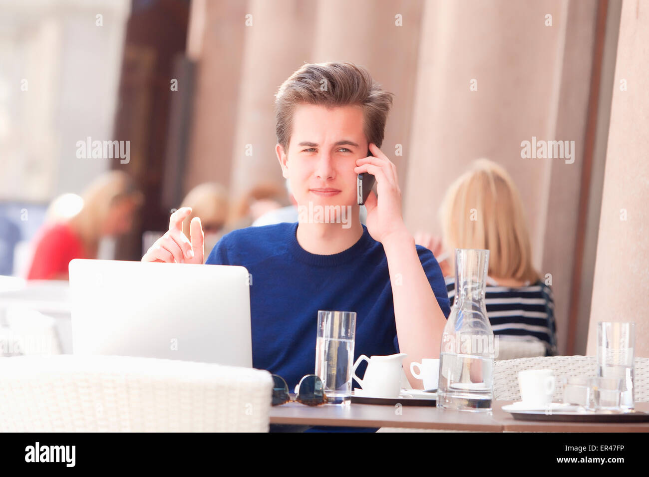 Junger Mann sitzt im äußeren Kaffeehaus reden über Handy Stockfoto