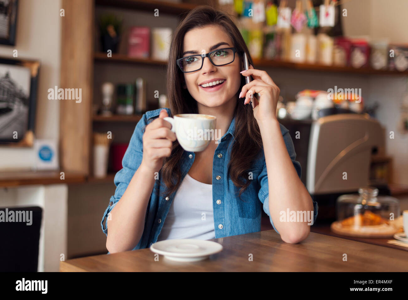 Lächelnde junge Frau im Gespräch mit dem Handy im Café. Krakau, Polen Stockfoto