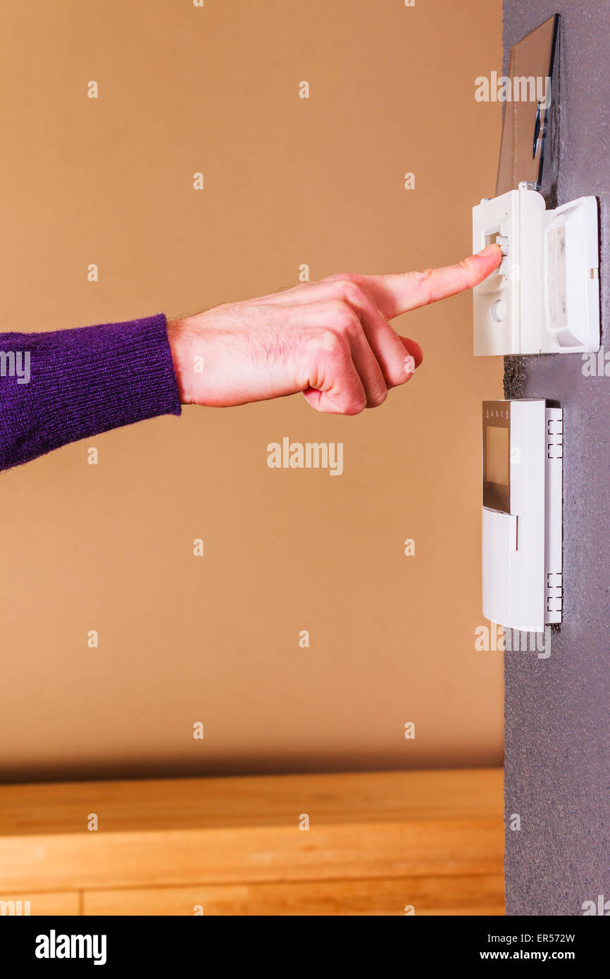 Junge männliche Hand Drücken der Taste der elektronische Thermostat an Wand des modernen Hauses. Sauberer Hintergrund Szene lila Wollpullover. Stockfoto
