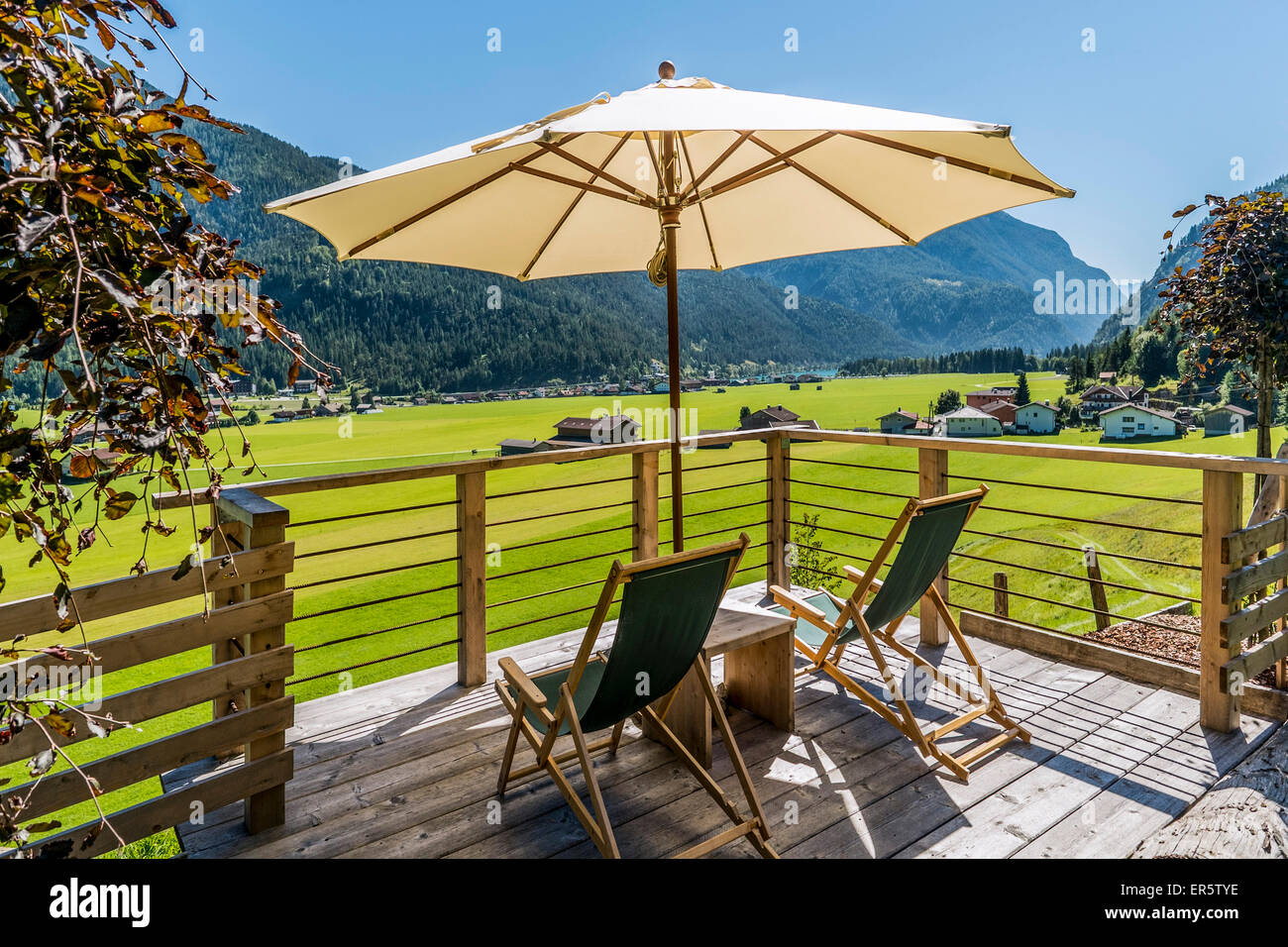 Liegestühle und Sonnenschirm auf der Terrasse, See Achensee und Achenkirch im Hintergrund, Tirol, Österreich Stockfoto