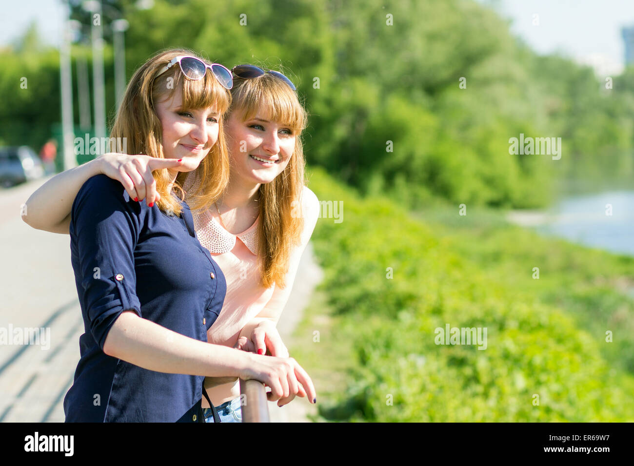 Hübsche Zwillinge Mädchen, die Spaß am wegsehen kopieren im freien Raum. Jung lächelnd kaukasische Frauen schauen auf Fluß an sonnigen Sommer da Stockfoto